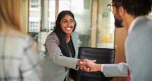 Young woman shakes the hand of a man in a suit after securing a new job.