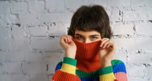 Shy girls pulls the neck of her sweater over her nose to hide